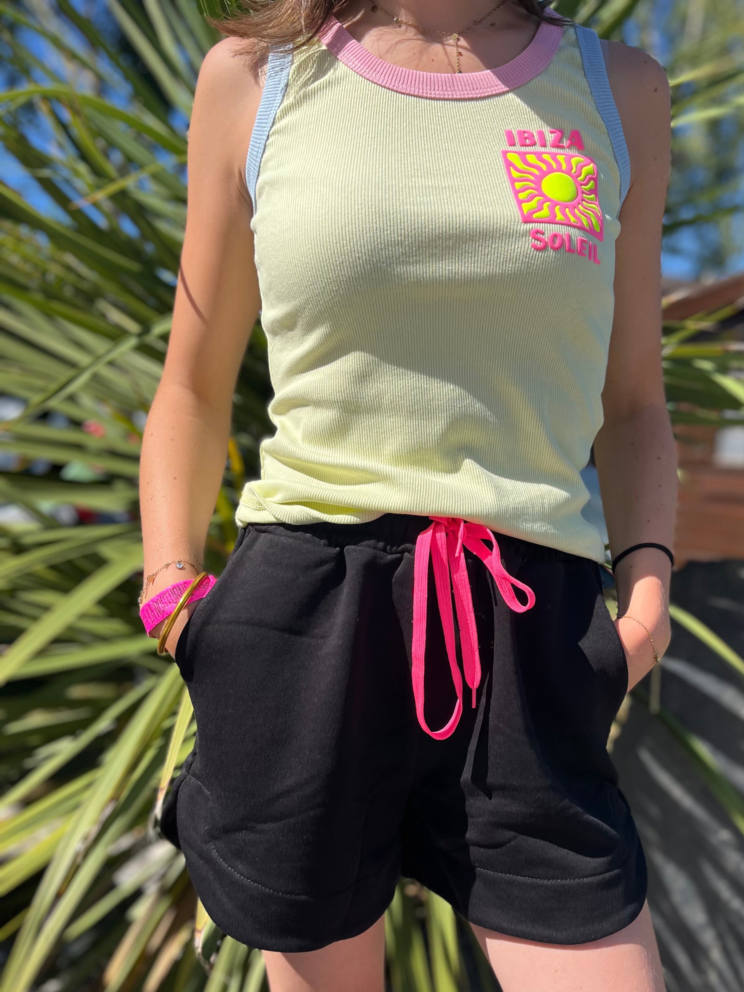 Look estival femme – débardeur Ibiza Soleil jaune pastel avec short noir serrage rose fluo, style bohème chic en extérieur